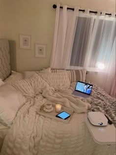 an unmade bed with two laptops on top of it next to a window