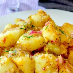 a white plate topped with potatoes covered in seasoning and sprinkled with herbs