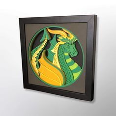 a green and yellow paper cut dragon in a black frame on the wall next to a white wall