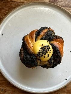 a pastry with yellow icing and black sprinkles on a white plate