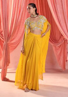 Dazzle in this enchanting ensemble: an embellished choli paired seamlessly with an embellished cape, adding a touch of drama and elegance. Complete the look with a draped skirt for effortless grace and sophistication, perfect for any glamorous affair. Yellow Dhoti Dress For Haldi Function, Yellow Festive Sets With Cape Sleeves, Festive Yellow Sets With Cape Sleeves, Festive Draped Lehenga With Resham Embroidery, Festive Draped Resham Embroidery Lehenga, Diwali Draped Sets With Dupatta, Draped Georgette Dress With Zari Work, Festive Draped Sharara With Sheer Dupatta, Designer Anarkali Draped Lehenga