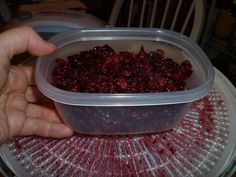 a plastic container filled with cranberries sitting on top of a table next to a person's hand