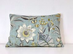 a blue pillow with white flowers and green leaves on the front, against a white wall