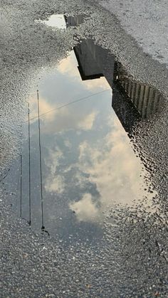 there is a reflection of the sky and clouds in the wet pavement on this street