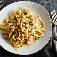 a plate of pasta with meat and parsley on it next to a glass of wine