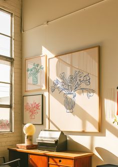 a room with a desk, chair and pictures on the wall above it in front of a window