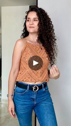 a woman standing in front of a mirror wearing jeans and a top with a button on it