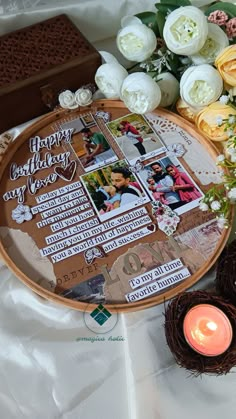 a table topped with flowers and pictures next to a lit candle on top of a white sheet