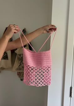 a woman holding a pink crocheted bag in front of a white closet door