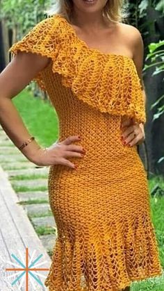 a woman wearing a yellow crochet dress standing on a wooden deck in the grass