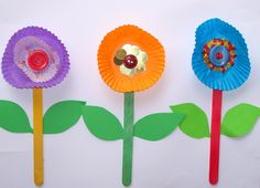 three paper flowers on sticks with green leaves