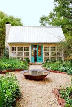 a small house with a blue door in the middle of a gravel path and lots of greenery