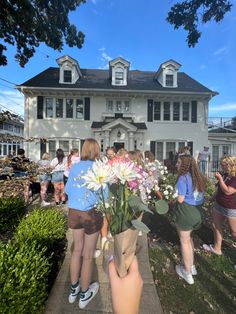 a group of people standing in front of a large white house with lots of flowers