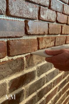 a hand is holding a piece of paper in front of a brick wall that has been built into it