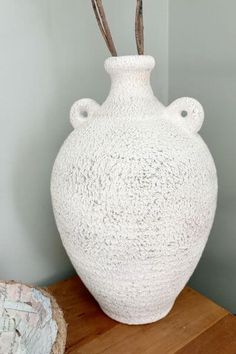 a large white vase sitting on top of a wooden table next to a tree branch