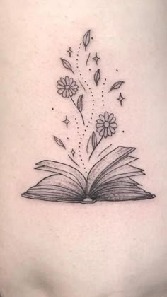 an open book with flowers coming out of it on the back of a woman's stomach