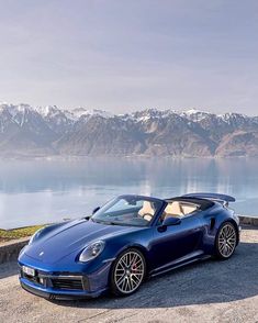 a blue sports car parked on the side of a road next to a body of water