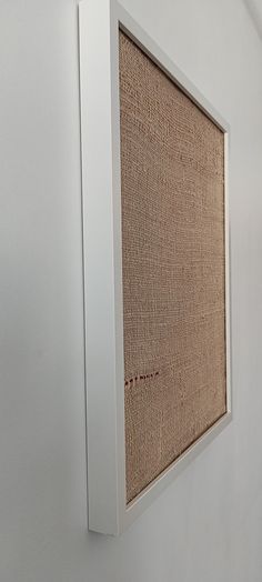 a white frame hanging on the side of a wall with a piece of cloth in it