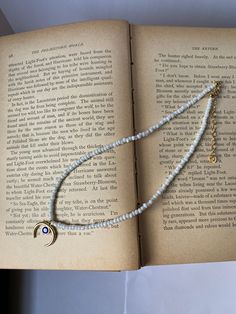 an open book with a white beaded necklace on it's cover and a crescent charm