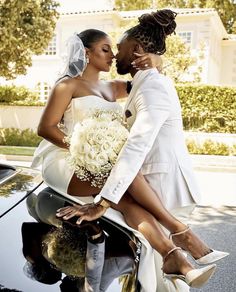 a bride and groom sitting on the hood of a car