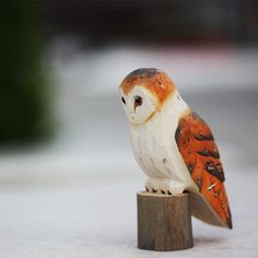 an orange and white owl figurine sitting on top of a piece of wood