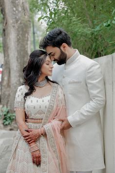 a man and woman standing next to each other in front of some trees wearing white outfits