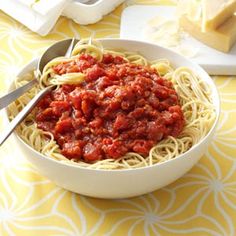 a white bowl filled with spaghetti and sauce on top of a yellow table cloth next to cheese