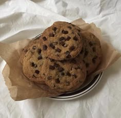 three chocolate chip cookies sitting on top of a black and white plate next to a brown paper bag