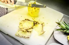 a person cutting up food on top of a white cutting board next to a pineapple