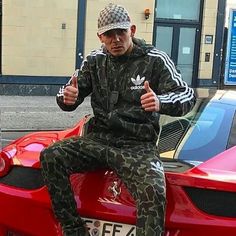 a man sitting on top of a red sports car giving the thumbs up sign with his hand