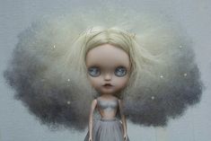 a doll with blonde hair and blue eyes standing in front of a white wall wearing a gray dress