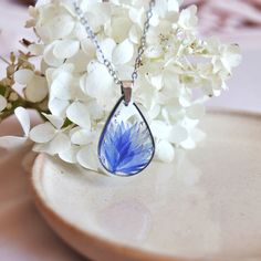 a necklace with a blue flower in the center on a plate next to white flowers