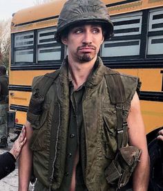 a man in an army uniform standing next to a school bus