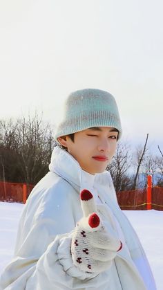 a young boy is standing in the snow wearing a white coat and a knitted hat