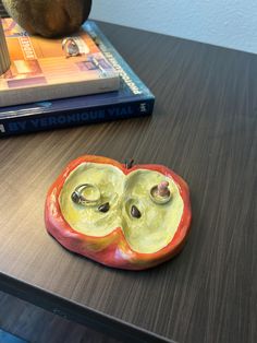 an apple shaped brooch sitting on top of a table next to a stack of books