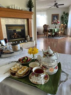 a table topped with tea cups and plates filled with food next to a fire place