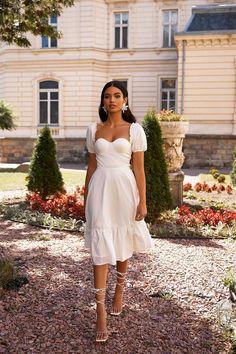 a woman standing in front of a building wearing a white dress and high heeled sandals