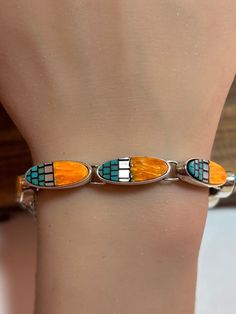 This is a beautiful, vintage, genuine Waldeck Jewelry multi stone and sterling silver bracelet that features natural blue turquoise, orange spiny oyster, and white Mother of Pearl / MOP. The bracelet is 7 inches.  The bracelet features 7 links each with the inlaid orange spiny oyster, rectangular-cut blue turquoise and white Mother of Pearl / MOP with black resin between the stones. Each link measures about 3/4" in length by a little more than 1/4" in width at the widest point. The stones are vibrant and the bracelet is very unique and well made. The bracelet is a little more than 1/4" in width at the widest point. It has some natural patina - a testament to its age - which its new owner can clean off if so desired. The bracelet weighs about 21.3 grams and is stamped 925 WJ, which is the h Southwestern Sterling Silver Inlay Bracelet Gift, Southwestern Oval Bracelets As Gift, Southwestern Oval Bracelets For Gift, Southwestern Style Oval Bracelets As Gift, Southwestern Style Oval Bracelets For Gifts, Southwestern Style Oval Bracelet Gift, Sterling Bracelets, Black Resin, Spiny Oyster