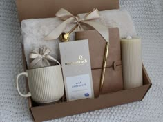 an open box with coffee, candles and other items in it on a white blanket