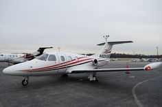 two small airplanes parked on the tarmac at an airport with other planes in the background