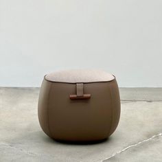 a small stool with a square seat on it's side, in front of a white wall