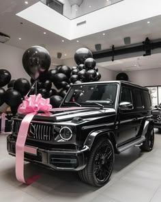 a black car with a pink ribbon tied to it's front and balloons behind it