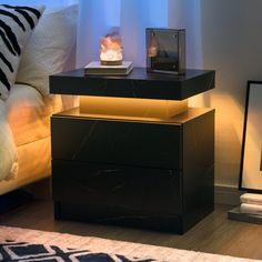 a night stand with a lamp on it next to a bed and a framed photograph