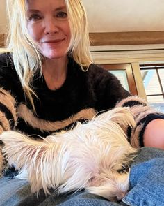 a woman sitting on top of a couch holding a small white dog in her lap