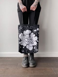 a person holding a black and white flower tote bag with tattoos on their arms