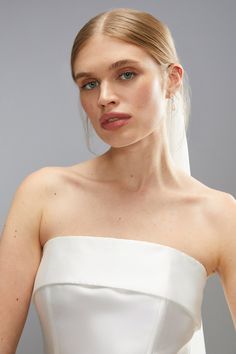 a woman wearing a white wedding dress with her hair in a pony tail style bun