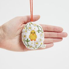 a hand holding an ornament with a yellow bird on it