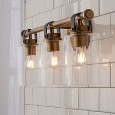 three light fixtures mounted on a white tiled wall in a bathroom with glass blocks and metal fittings