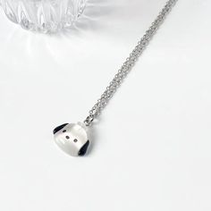 a white and black panda bear necklace on a silver chain with a clear glass vase behind it