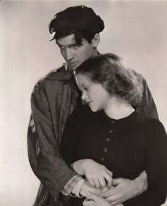 an old black and white photo of a man standing next to a young woman with her arms around him